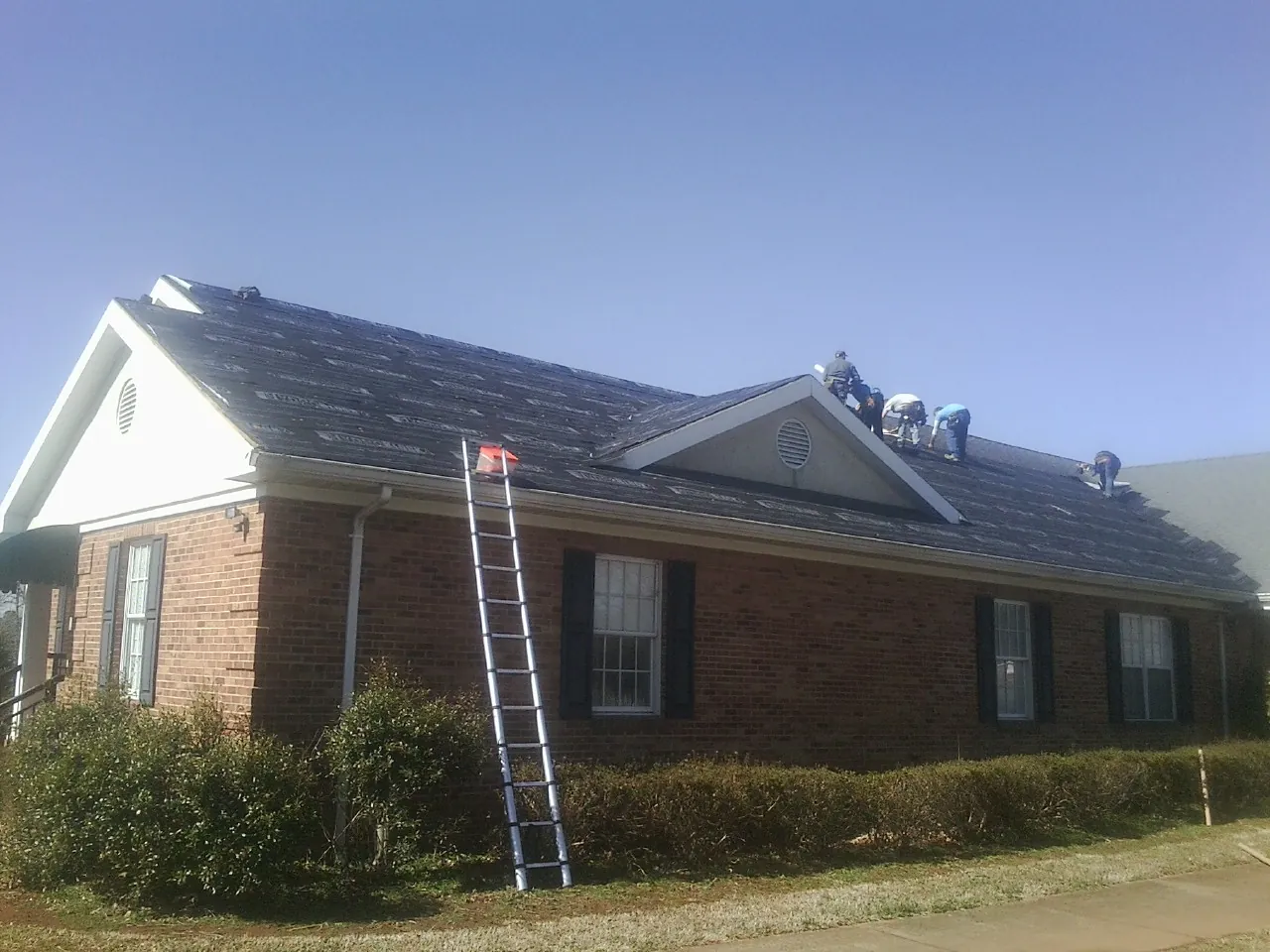 Crew tearing shingles off a brick ranch roof with a ladder set — Emergency Roof Repair work by our crew in Eden Valley