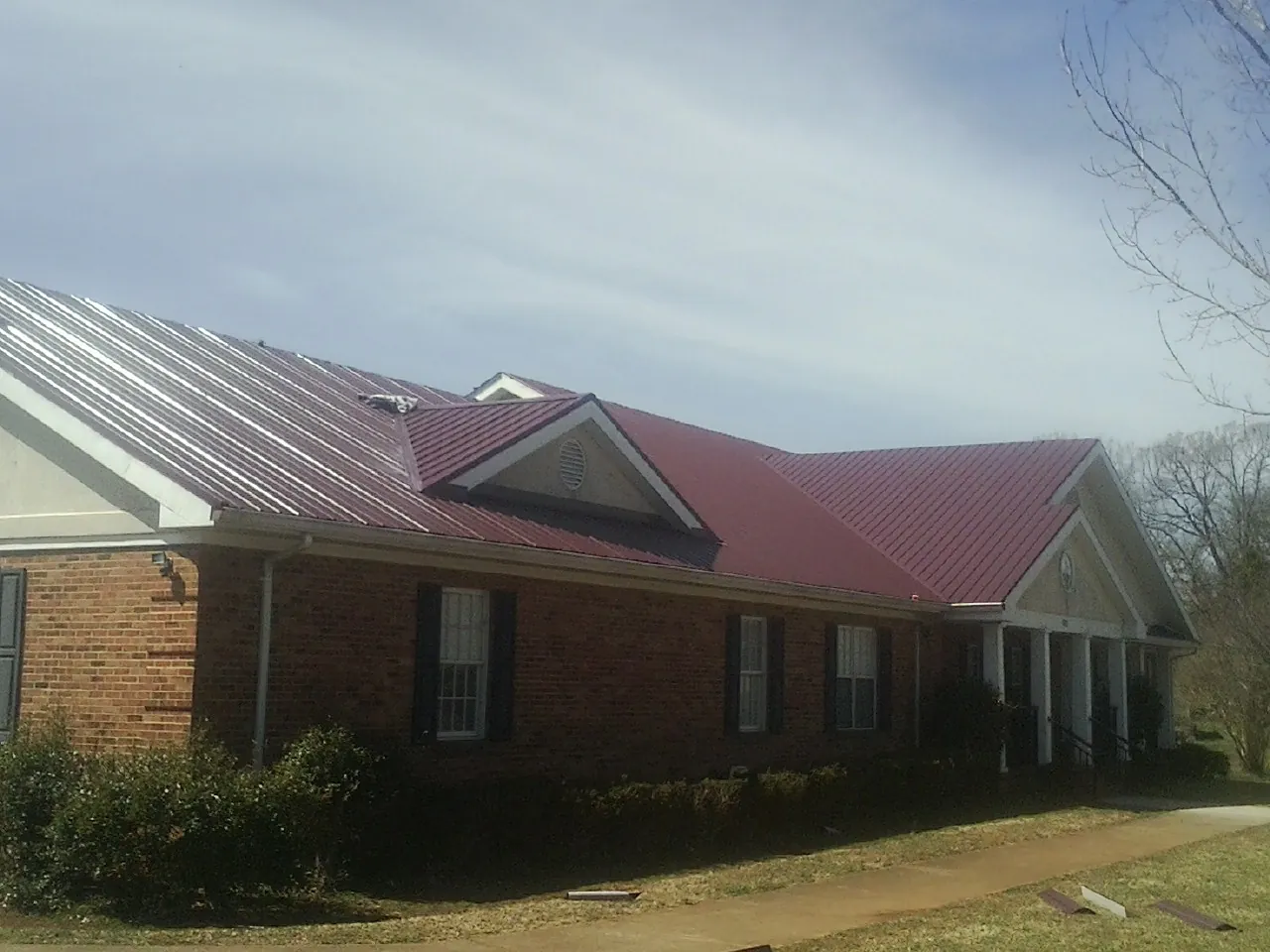 Red metal roof with gabled entries on a long brick building, from a Hail Damage Roof Repair job in Eden Valley