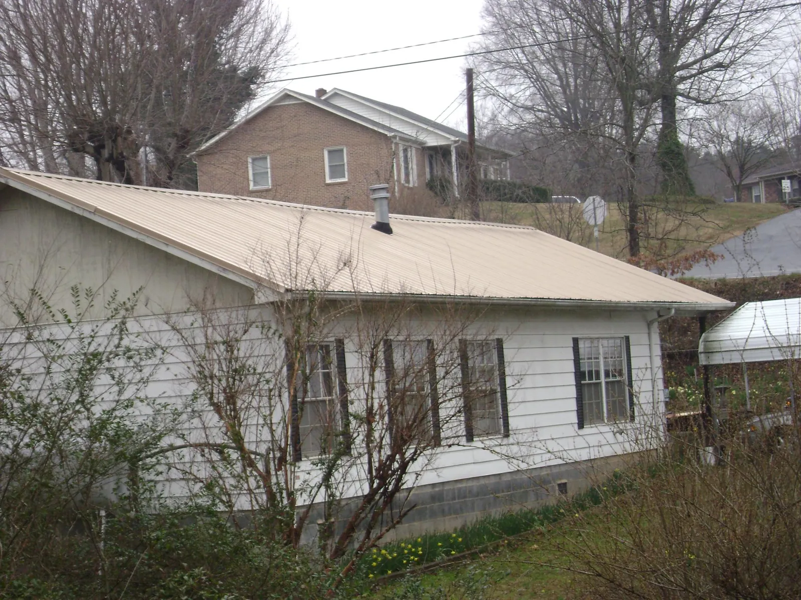 Tan metal roof on a white sided house set into a hillside — Commercial Roofing by Roofing Brothers in Eden Valley